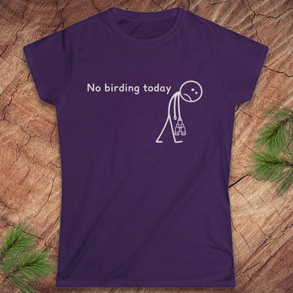 A purple short-sleeve crewneck t-shirt with a white graphic print that reads 'No birding today' next to a stick figure carrying a birdhouse. The shirt is laid flat on a textured wood background with pine needles in the corners.