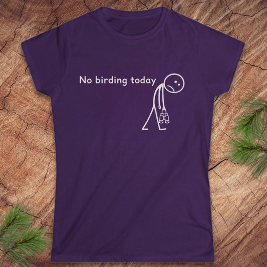 A purple short-sleeve crewneck t-shirt with a white graphic print that reads 'No birding today' next to a stick figure carrying a birdhouse. The shirt is laid flat on a textured wood background with pine needles in the corners.
