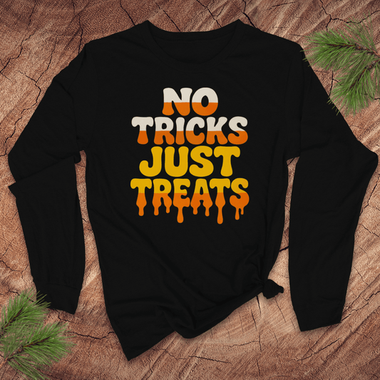 Black long sleeve tshirt with 'No Tricks Just Treats' text on a wooden surface with pine branches.