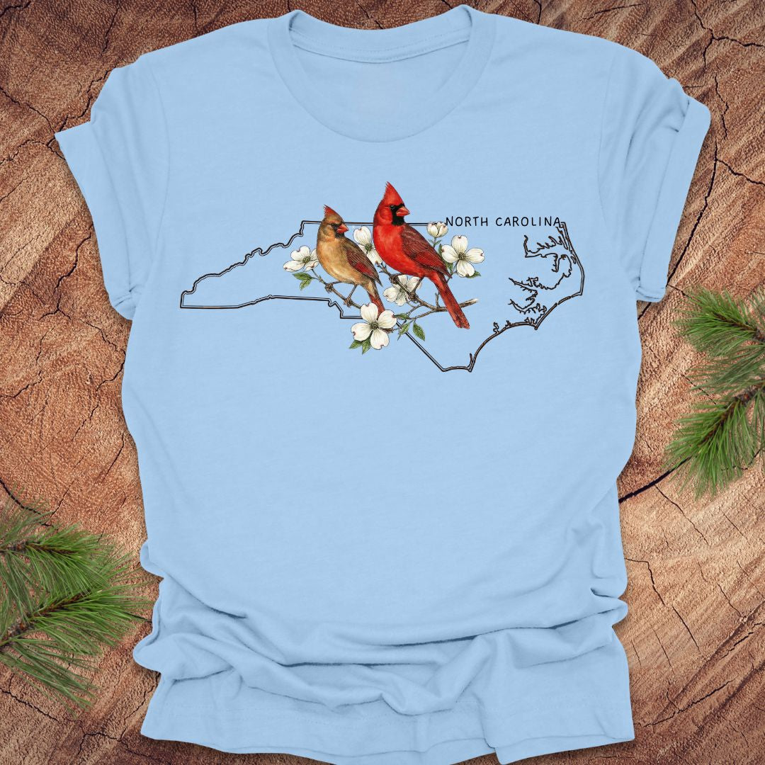 Light blue t-shirt with north carollina state map and cardinal design on a wooden surface