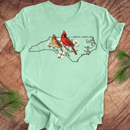 Mint green t-shirt with North Carolina map and cardinals design on a wooden surface.