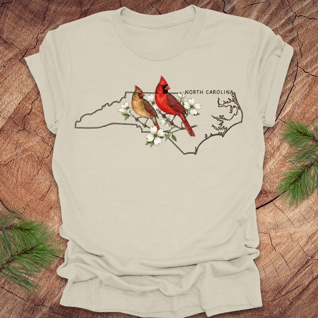Beige t-shirt with North Carolina map and cardinals design on a wooden surface