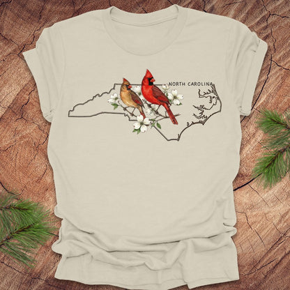 Beige t-shirt with North Carolina map and cardinals design on a wooden surface