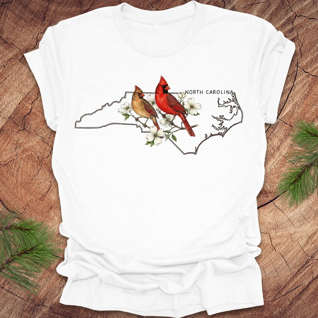 White t-shirt with North Carolina map and cardinals design on a wooden surface