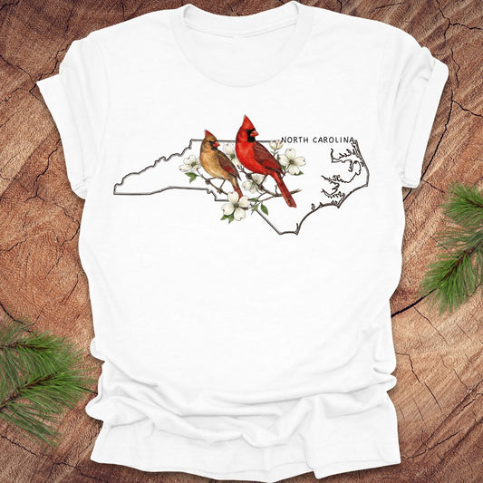 White t-shirt with North Carolina map and cardinals design on a wooden surface