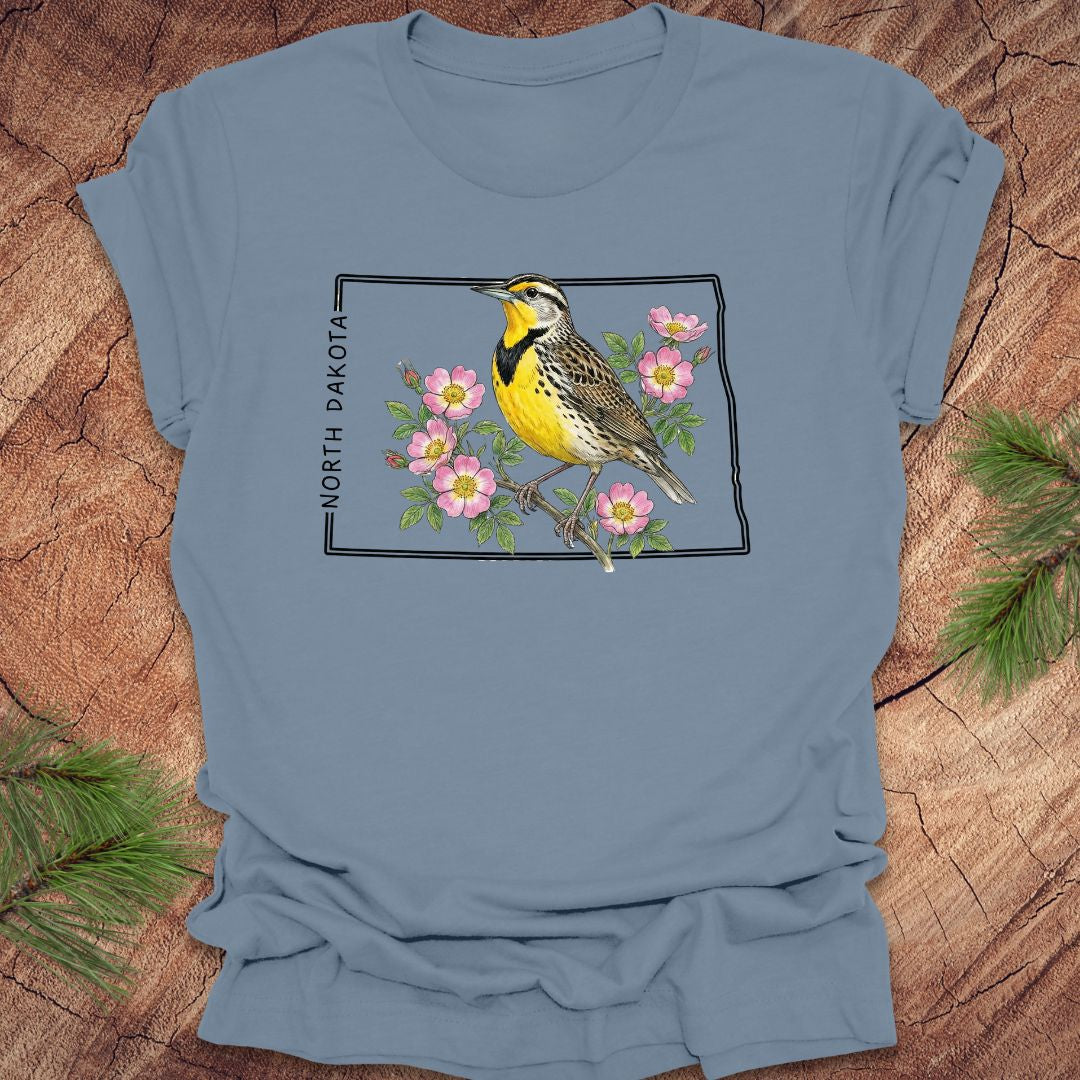 Steel blue t-shirt with a meadowlark and prairie rose flower inside the outline of North Dakota on a wooden surface
