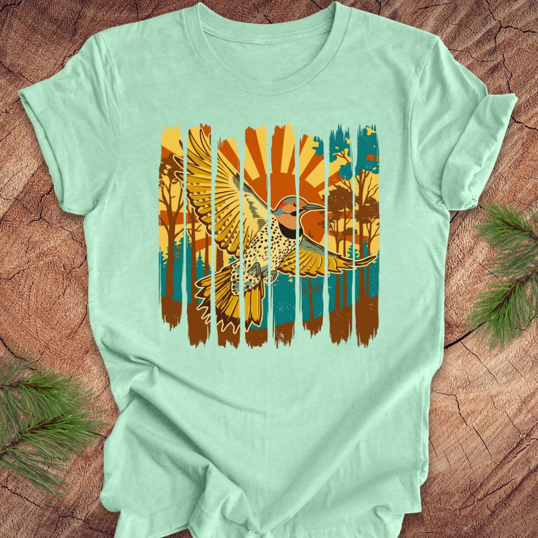 Mint green t-shirt with a colorful graphic of a northern flicker and nature elements on a wooden surface.