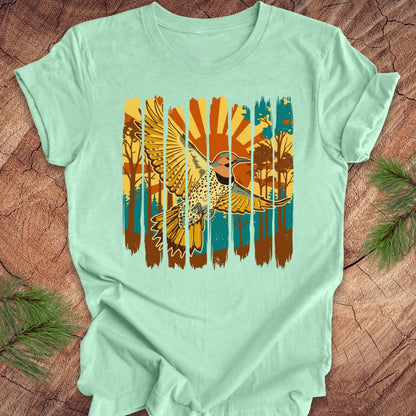 Mint green t-shirt with a colorful graphic of a northern flicker and nature elements on a wooden surface.
