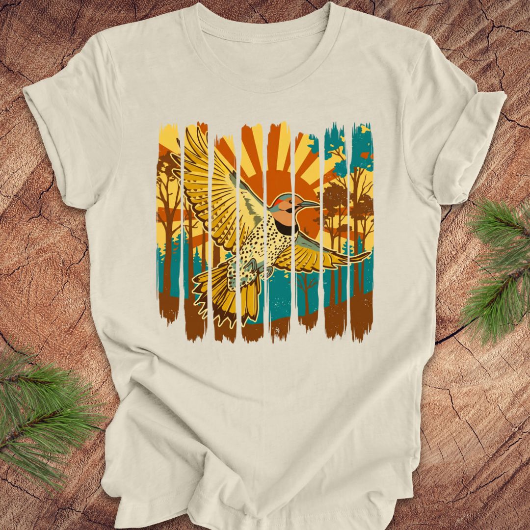 Beige t-shirt with a colorful graphic of a northern flicker and nature elements on a wooden surface.