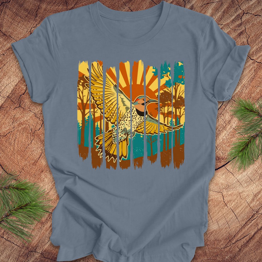 Blue t-shirt with a colorful graphic of a northern flicker and nature elements on a wooden surface.