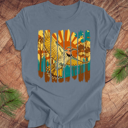 Blue t-shirt with a colorful graphic of a northern flicker and nature elements on a wooden surface.