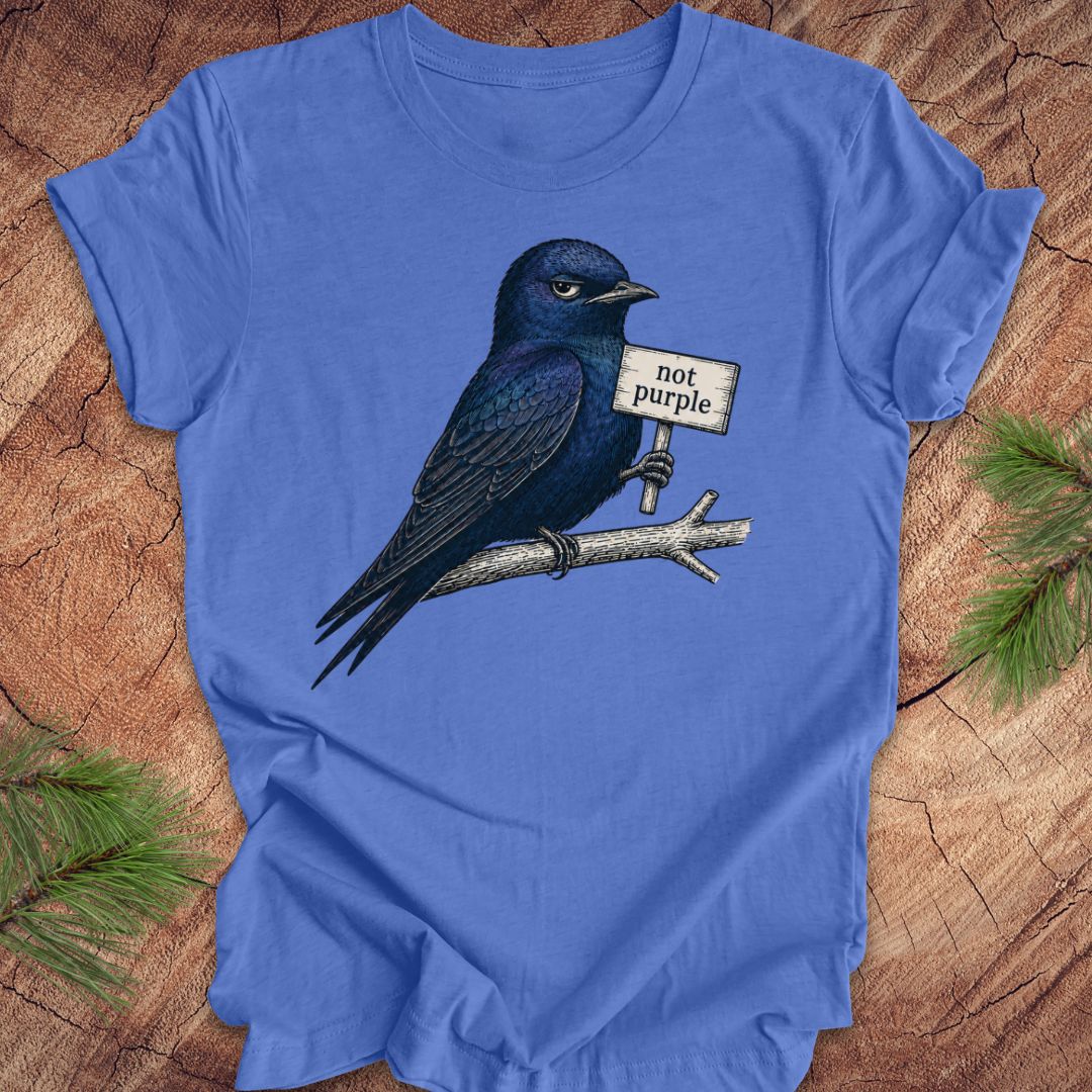 Blue t-shirt with a bird holding a 'not purple' sign on a wooden surface.