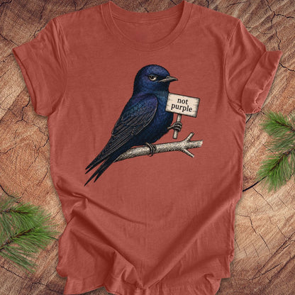 Red t-shirt with a purple martin bird graphic and 'not purple' sign on a wooden surface.
