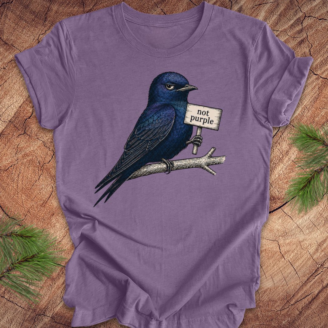 Purple t-shirt with a purple martin bird holding a sign saying 'not purple' on a wooden surface.
