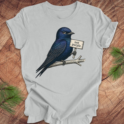 Gray t-shirt with a purple martin bird holding a 'not purple' sign on a wooden surface.