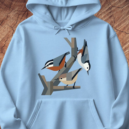 A light blue pullover hoodie featuring a stylized graphic print of three birds perched on branches, displayed flat against a textured brown wood background.
