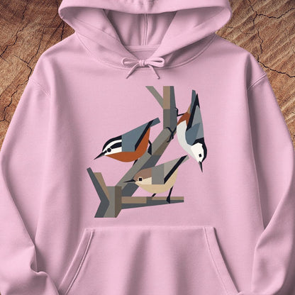 A light pink pullover hoodie featuring a stylized geometric graphic of three birds perched on branches on the chest, displayed flat against a rustic wood background.