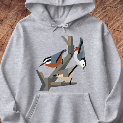 A light heather gray pullover hoodie featuring a stylized graphic of three birds perched on branches on the chest, displayed against a rustic wood background.
