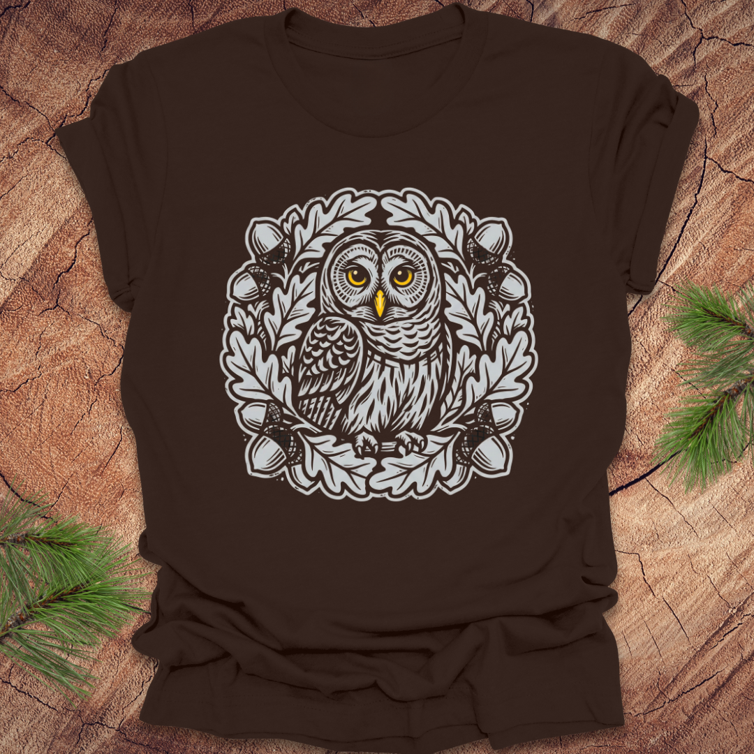 Brown t-shirt with an owl in an oak tree design on a wooden surface