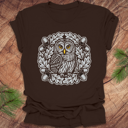 Brown t-shirt with an owl in an oak tree design on a wooden surface