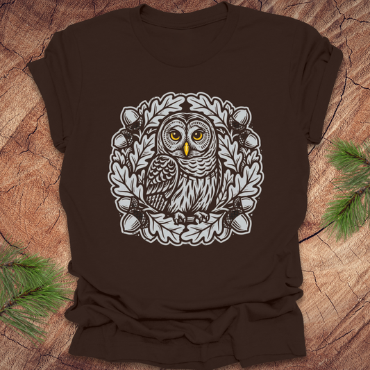 Brown t-shirt with an owl in an oak tree design on a wooden surface