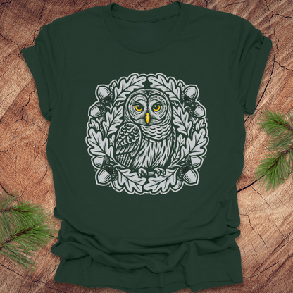 Green t-shirt with an owl in an oak tree design on a wooden surface