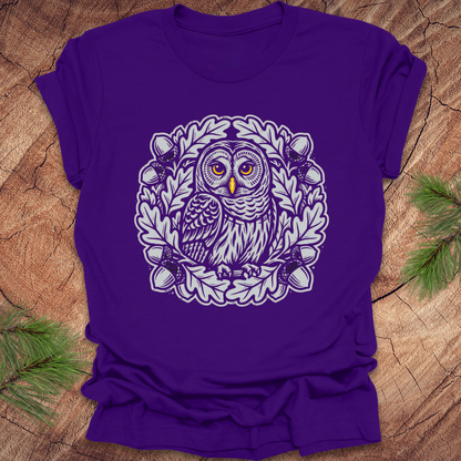 Purple t-shirt with an owl in an oak tree design on a wooden surface
