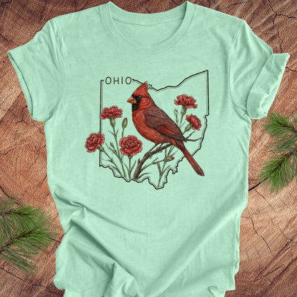 Light green t-shirt with a cardinal and floral design on an Ohio map, placed on a wooden surface.