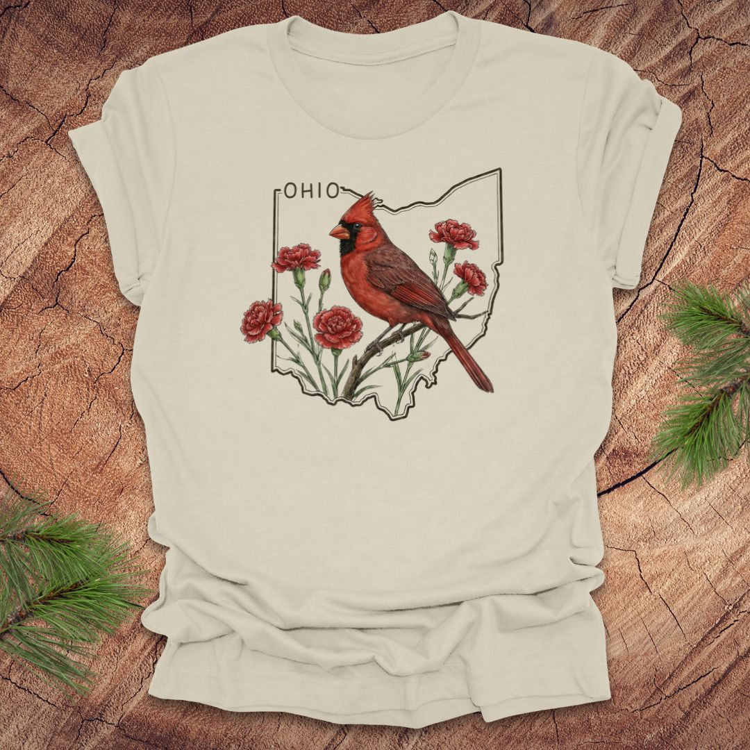 Beige t-shirt with a cardinal and floral design on an Ohio map, placed on a wooden surface.
