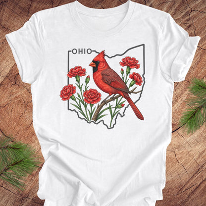 A white short-sleeve T-shirt laid flat on a rustic wood surface, featuring a printed graphic of a red cardinal bird over the outline of Ohio with red flowers and the word "OHIO" at the top.