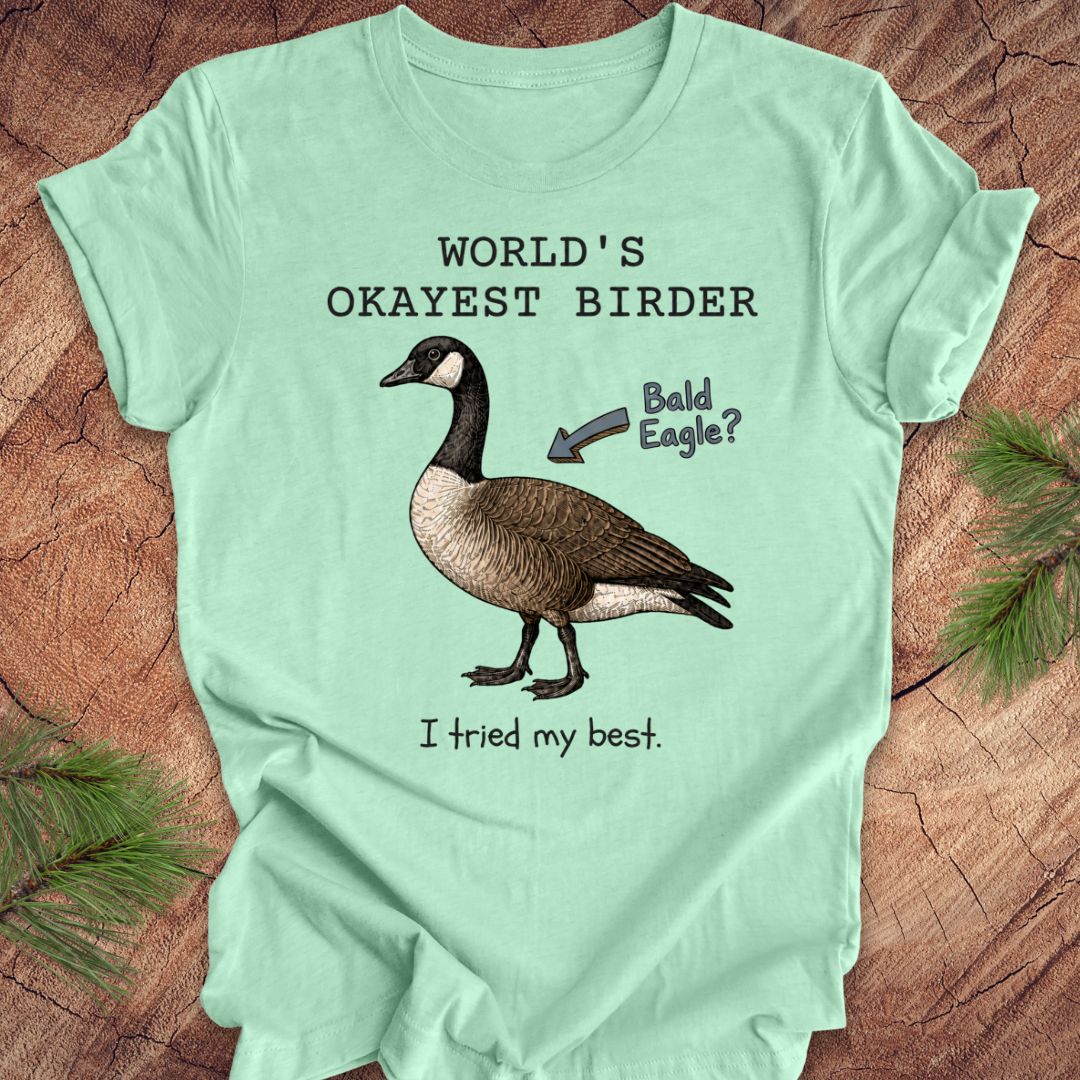 Light green t-shirt with a goose graphic and text on a wooden surface