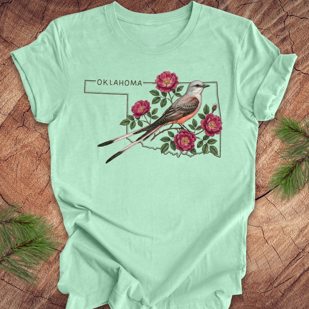 Mint green t-shirt with state bird, scissor-tailed flycatcher and rose, on an Oklahoma map, placed on a wooden surface.