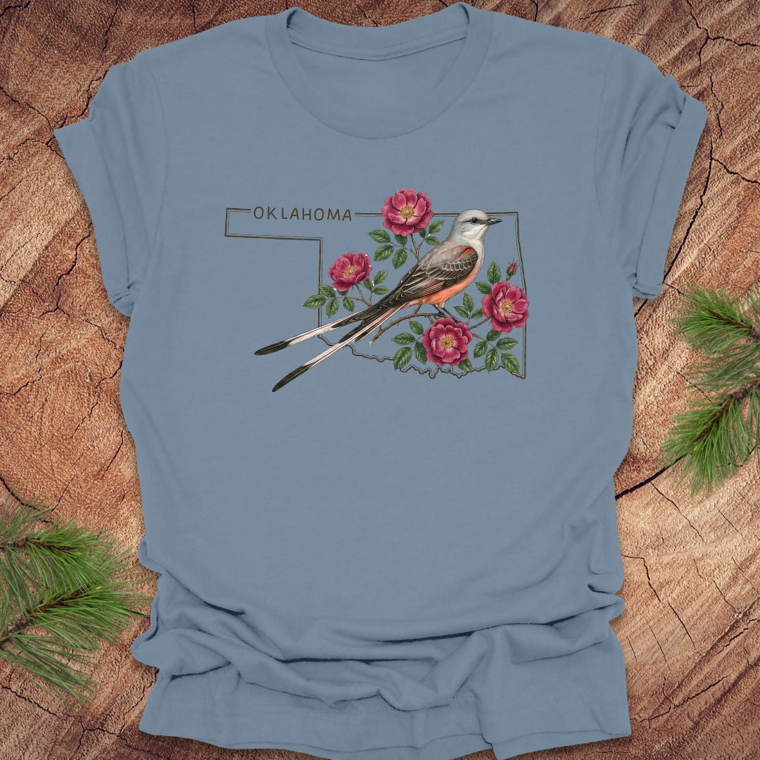 Steel blue t-shirt with state bird, scissor-tailed flycatcher and rose, on an Oklahoma map, placed on a wooden surface.