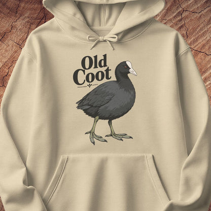 A beige hoodie laid flat on a textured brown wood background, featuring a printed graphic of an old coot bird with the text 'Old Coot' above it.