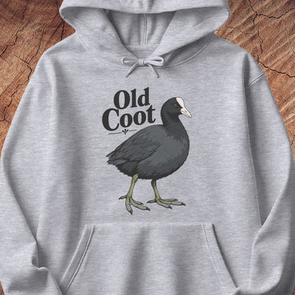 A light heather gray pullover hoodie featuring a graphic print of an American coot bird and the text 'Old Coot' in black. The hoodie is displayed flat against a rustic wood background.