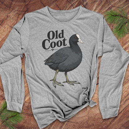 A heather gray long-sleeve t-shirt with a graphic of a dark gray coot bird and the text 'Old Coot' printed on the front, styled flat on a rustic wood background with pine needles.