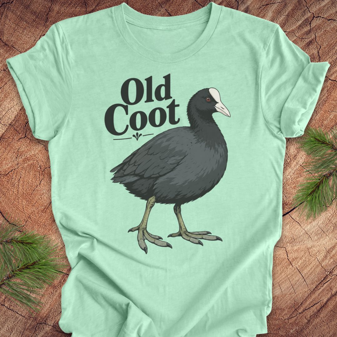 A mint green short-sleeve t-shirt laid flat on a rustic wood surface, featuring a graphic of a dark coot bird and the text 'Old Coot'.