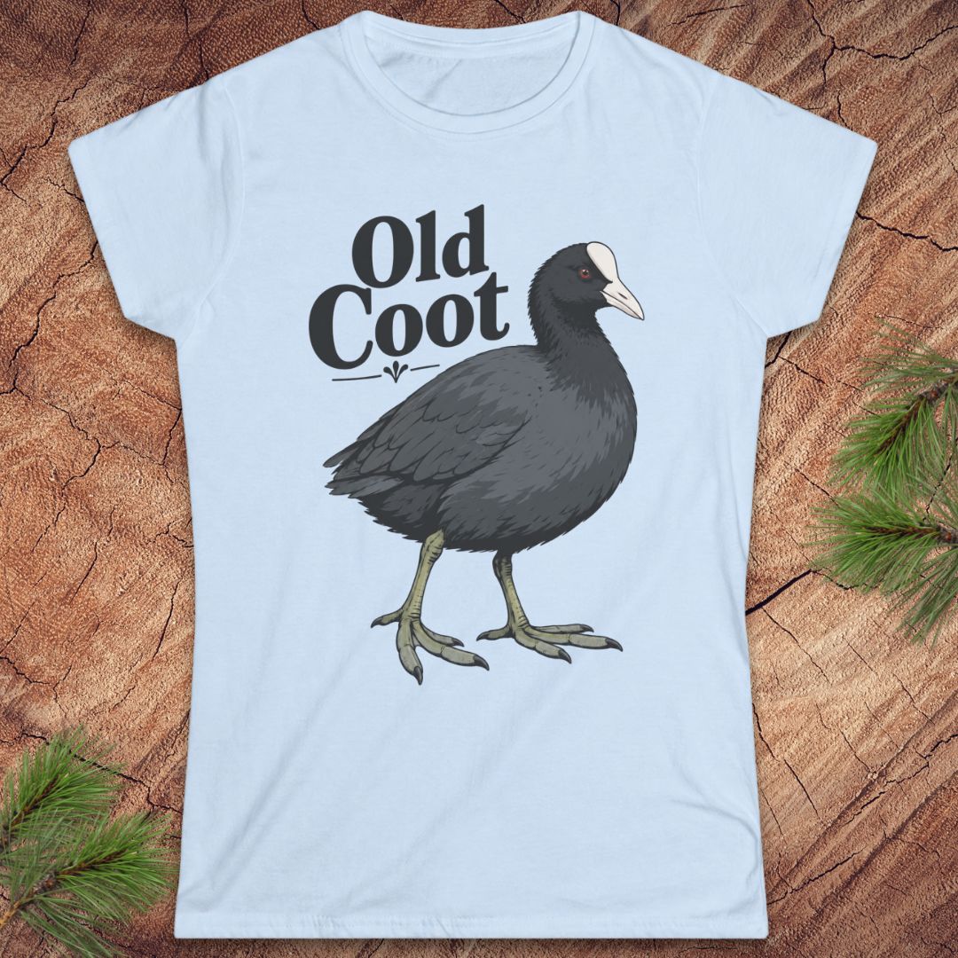 A light blue short-sleeve t-shirt with a graphic of an 'Old Coot' bird and text, displayed flat on a rustic wood background with pine branches.