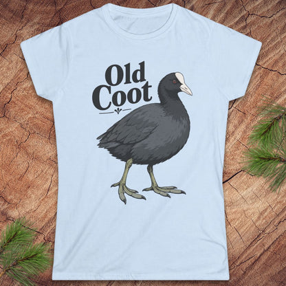 A light blue short-sleeve t-shirt with a graphic of an 'Old Coot' bird and text, displayed flat on a rustic wood background with pine branches.
