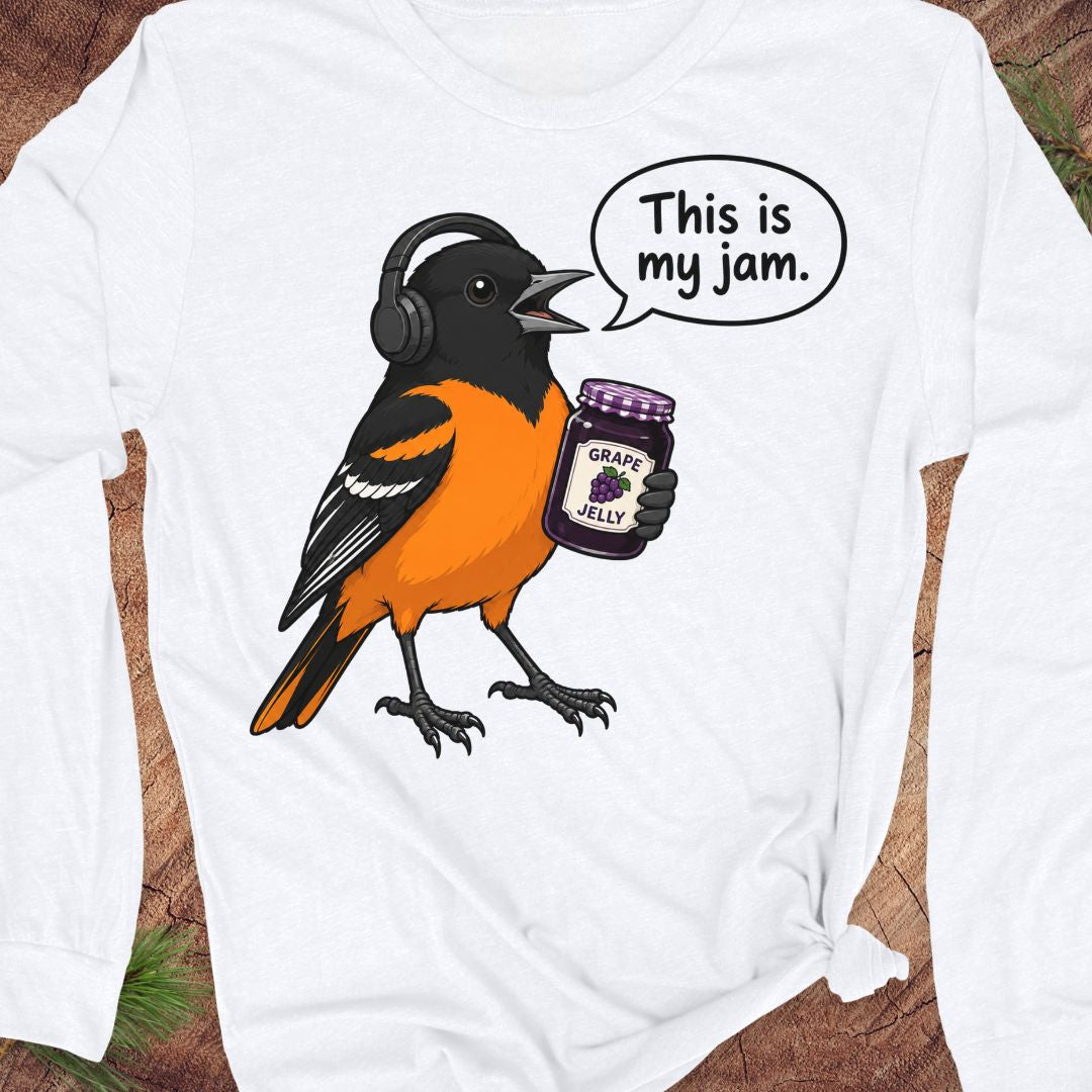 A white long-sleeve t-shirt with a graphic of an orange and black bird wearing headphones and holding a jar of grape jelly, with a speech bubble that reads 'This is my jam.' The shirt is laid flat on a rustic wood background.