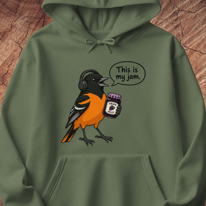 An olive green pullover hoodie featuring a cartoon graphic of an orange and black bird wearing headphones and holding a jar of jam with the text 'This is my jam.' printed on the front, set against a textured wood background.
