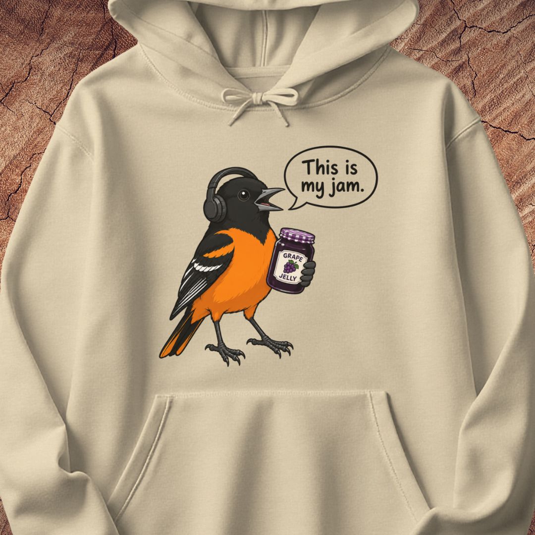 A beige hoodie featuring a cartoon bird wearing headphones and holding a jar of 'Grape Jelly' with a speech bubble that reads 'This is my jam.' The hoodie is displayed flat against a textured brown wood background.