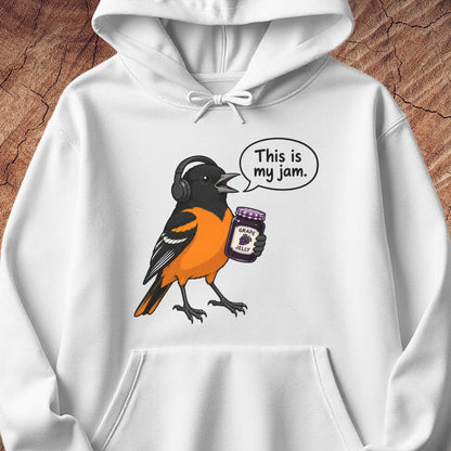 A white pullover hoodie with a graphic of an orange and black bird wearing headphones and holding a jar of jam, with a speech bubble that reads 'This is my jam.' The hoodie is shown against a rustic wood background.
