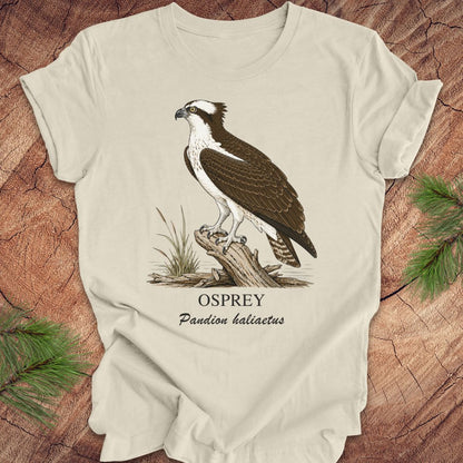 Beige t-shirt with osprey illustration and text on a wooden surface
