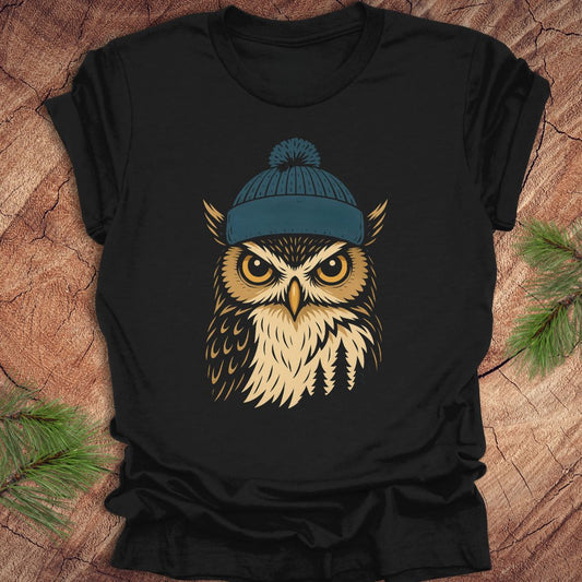 Black t-shirt with an owl wearing a blue beanie on a wooden surface.