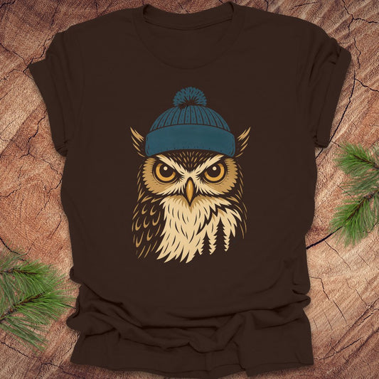 Brown t-shirt with an owl wearing a blue beanie on a wooden surface.