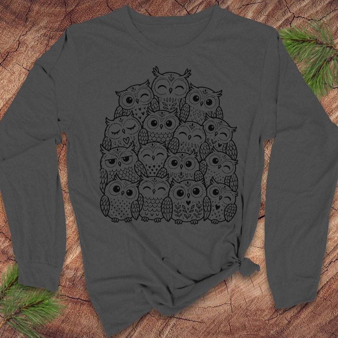 Asphalt gray long-sleeve t-shirt with a black line-art huddle of cute owls piled together, laid flat on a rustic wood background with pine branches.