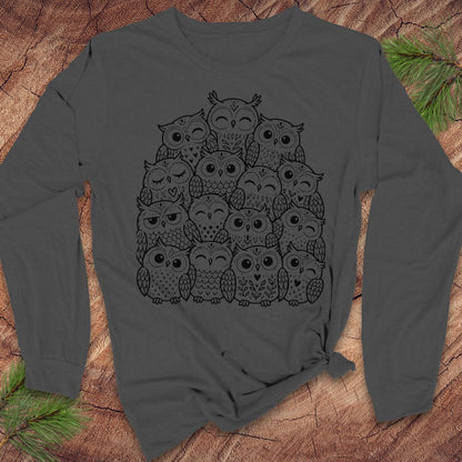 Asphalt gray long-sleeve t-shirt with a black line-art huddle of cute owls piled together, laid flat on a rustic wood background with pine branches.