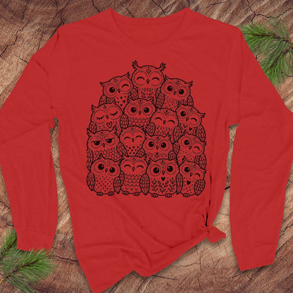 Red long-sleeve t-shirt with a black line-art huddle of cute owls piled together, laid flat on a rustic wood background with pine branches.