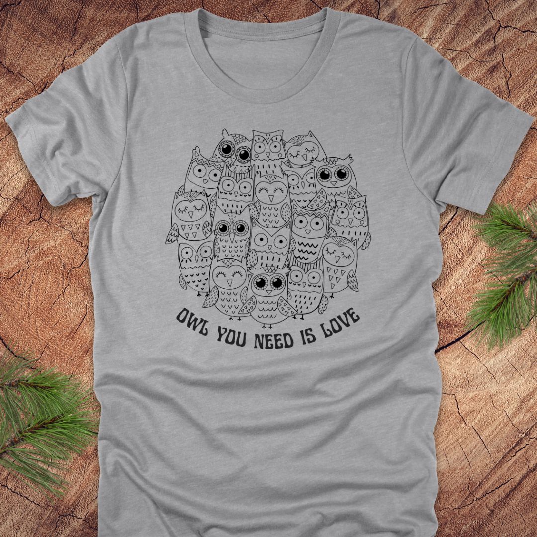 Grey t-shirt with owl design and text 'OWL YOU NEED IS LOVE' on a wooden surface.
